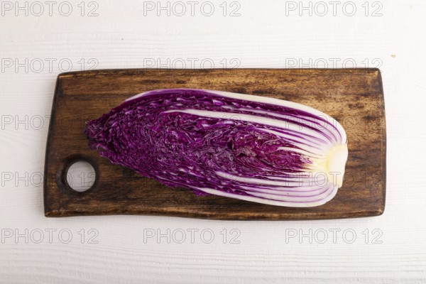 Purple Chinese cabbage on cutting board on white wooden background, top view, flat lay, close up, minimalism