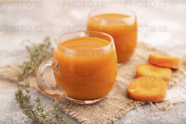 Two glasses with carrot juice, on brown concrete background and linen textile. Diet, healthy eating concept. side view, close up, minimalism, selective focus