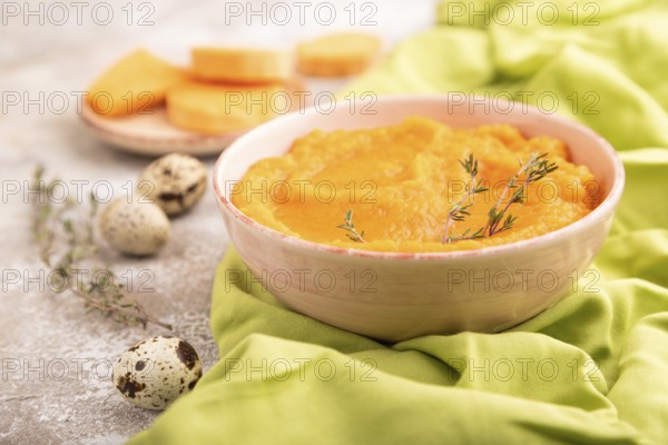 Sweet potato porridge in ceramic bowl on brown concrete background and green textile. Diet, healthy eating concept. side view, close up, selective focus