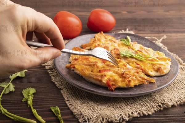 Baked chicken meat with cheese and tomatoes with hand on brown wooden background and linen textile. side view, close up, selective focus