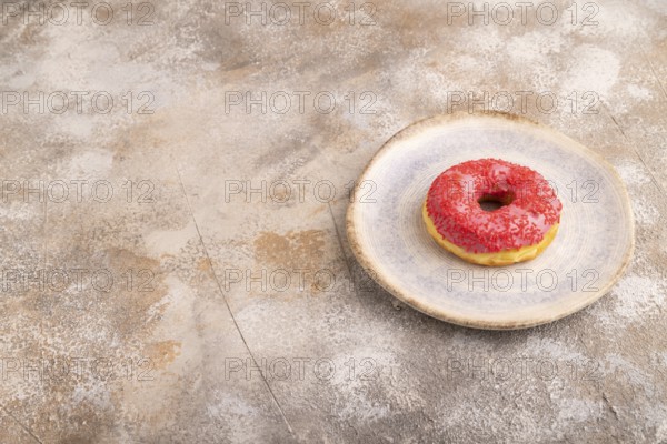 Pink Donut with sprinkles on blue ceramic plate on brown concrete background, side view, copy space, minimalism