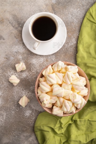 Orange and pink marshmallow in ceramic bowl on brown concrete background and green textile, top view, flat lay, close up, minimalism