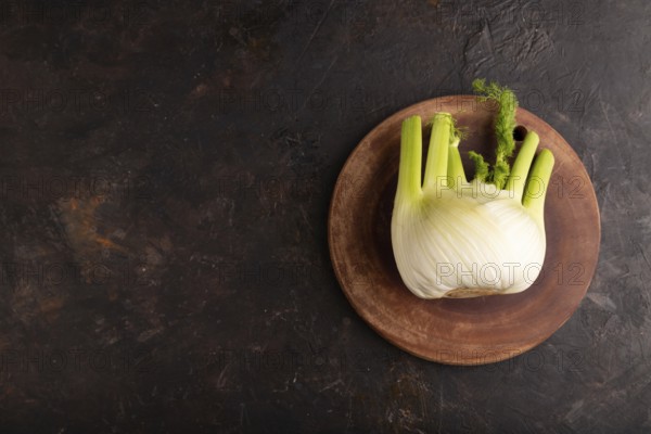 Fresh Fennel bulb on wooden cutting board on black concrete background, top view, flat lay, copy space, minimalism