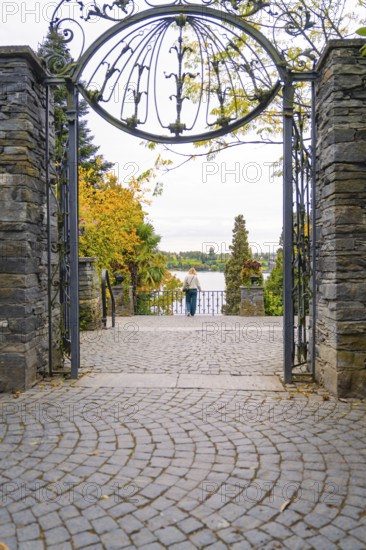 View through an ornate iron gate onto a cobbled driveway and a view beyond, Mainau Island, Lake Constance, Germany