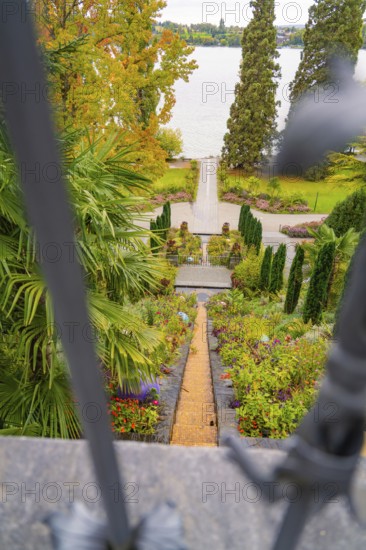View through a gate onto a well-kept garden path leading to the lake, surrounded by autumn trees, Mainau Island, Lake Constance, Germany