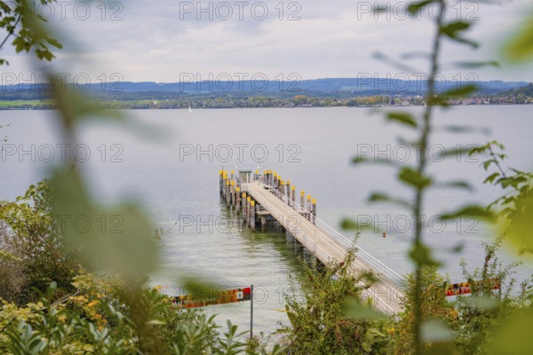 View of a long jetty leading into a calm lake with a cloudy sky in the background, Mainau Island, Lake Constance, Germany