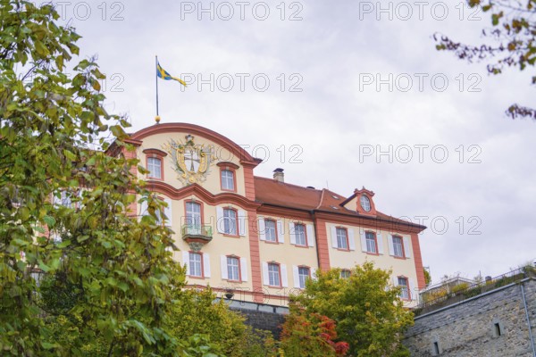 A magnificent building with a flag in the foreground, surrounded by autumnal greenery, Mainau Island, Lake Constance, Germany