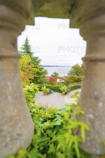 View through stone pillars of a landscape with trees and a large body of water, Mainau Island, Lake Constance, Germany