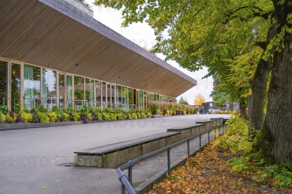 A modern building with large windows, surrounded by trees and falling leaves, Mainau Island, Lake Constance, Germany