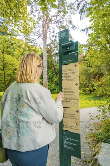 Woman standing in front of a signpost in autumn forest, Mainau flower island, Lake Constance, Germany