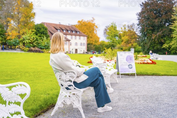 Woman sitting on a white garden bench, in the colourful autumn garden, Mainau flower island, Lake Constance, Germany