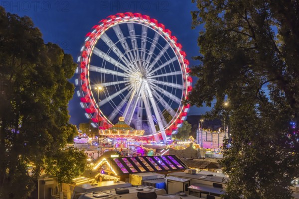 Folk festival in Stuttgart. The 178th Cannstatter Volksfest on the Wasen is one of the most important traditional festivals in Germany. Ferris wheel and other amusement park attractions, light effects at night. Stuttgart, Baden-Württemberg, Germany