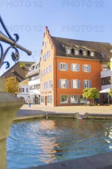 A fountain in the foreground with a striking historical building in the sunlight, Überlingen, Lake Constance, Germany