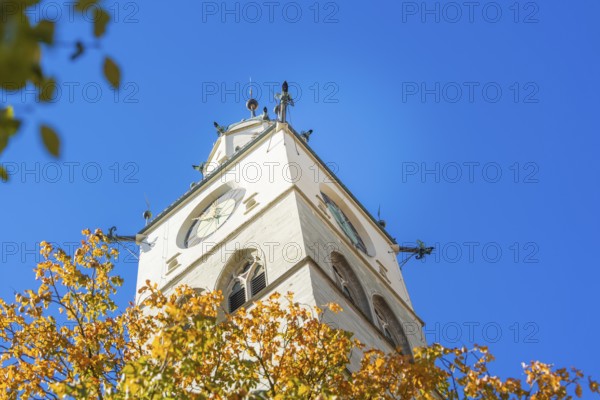A church tower with a clock, surrounded by autumn leaves in front of a clear blue sky, Überlingen, Lake Constance, Germany