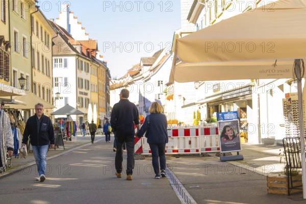 People walk along a sunny street, cafés and shops surround them, Überlingen, Lake Constance, Germany