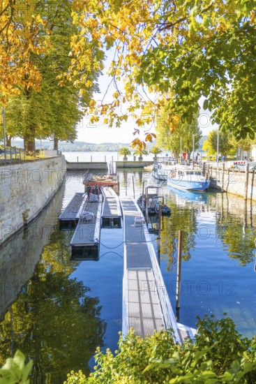 A jetty on the water in a small harbour, with autumnal trees on the shore, Überlingen, Lake Constance, Germany