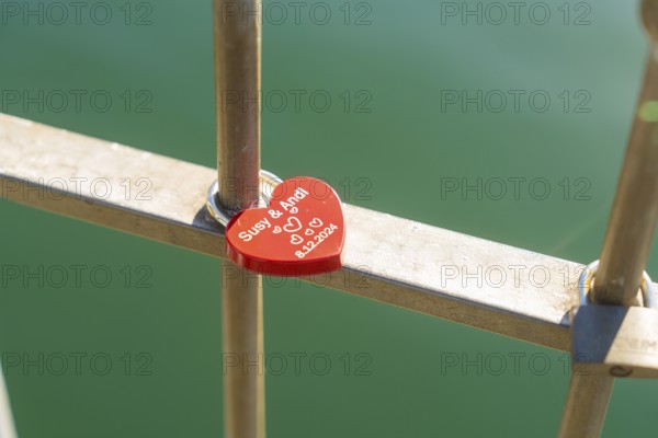 Red heart lock with engraving on the railing over green water, Überlingen, Lake Constance, Germany