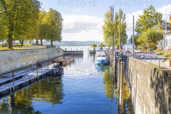 A small harbour with boats and autumnal trees on the shore, clear water, Überlingen, Lake Constance, Germany