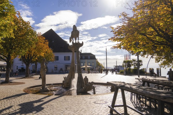 A sunny square with a fountain and autumnal trees, lined with buildings, Überlingen, Lake Constance, Germany