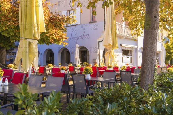 Cosy outdoor area of a café with red and black chairs, tables and large parasols in autumn light, Überlingen, Lake Constance, Germany