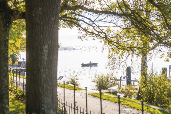 A peaceful lake with a boat in the water, seen from a shady path under trees, Überlingen, Lake Constance, Germany