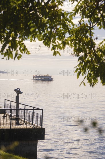 A boat passes by on a calm lake, visible from a binocular viewpoint next to a jetty, Überlingen, Lake Constance, Germany
