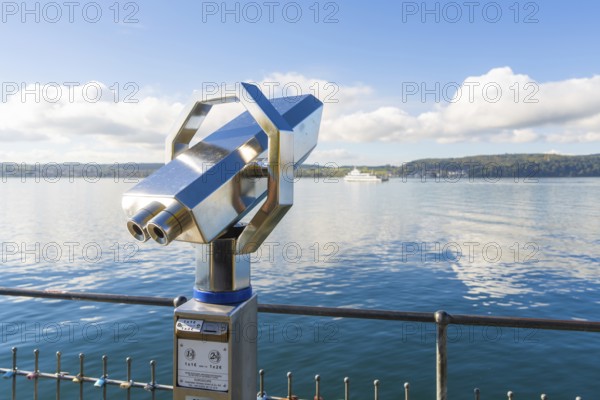 Metallic binoculars pointing to the lake with a peaceful view of the shore, Überlingen, Lake Constance, Germany