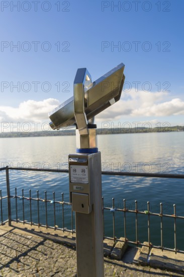 Binoculars on the lakeshore looking over calm water under a blue sky, Überlingen, Lake Constance, Germany