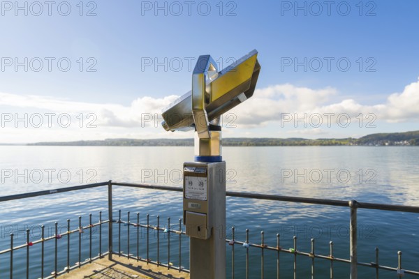 Binoculars on the shore pointing to a peaceful lake with blue sky and clouds, Überlingen, Lake Constance, Germany