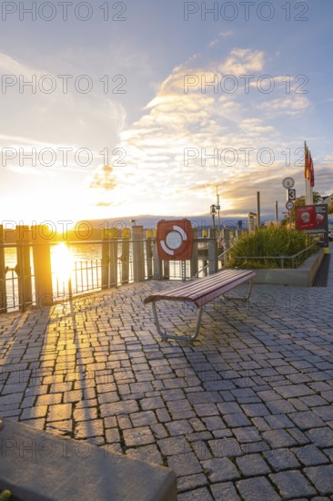 A sunny evening by the lake with an empty bench and a picturesque promenade, Überlingen, Lake Constance, Germany