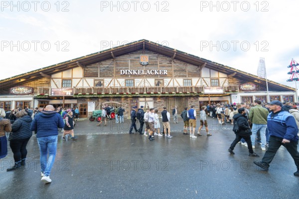 Visitors move in front of a large wooden building, lively atmosphere, Cannstatter Wasen folk festival, Stuttgart, Germany