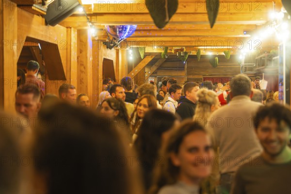 Cheerful atmosphere in an interior with wooden decor and lots of people, Cannstatter Wasen folk festival, Stuttgart, Germany