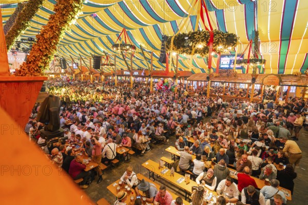 Large crowd celebrating in a colourfully decorated marquee, Cannstatter Wasen folk festival, Stuttgart, Germany