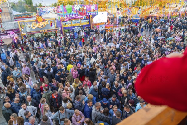 Dense crowd on a busy fairground with colourful attractions all around, Cannstatter Wasen funfair, Stuttgart, Germany