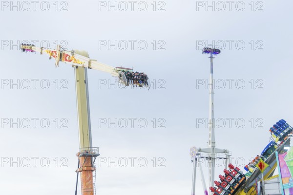 View of thrill rides with people high above and other attractions in the background, Cannstatter Wasen funfair, Stuttgart, Germany