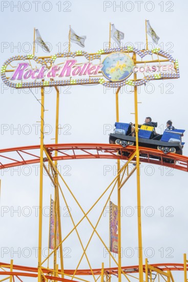 Passengers in a carriage on the roller coaster Rock'n'Roller Coaster under signs, Cannstatter Wasen funfair, Stuttgart, Germany