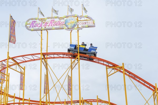 Colourful roller coaster with brave passengers on the rails in the amusement park, Cannstatter Wasen funfair, Stuttgart, Germany