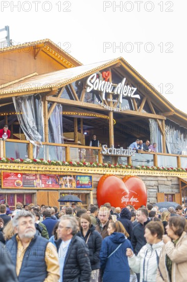 People on a balcony of a wooden building with a big heart in the foreground, Cannstatter Wasen folk festival, Stuttgart, Germany
