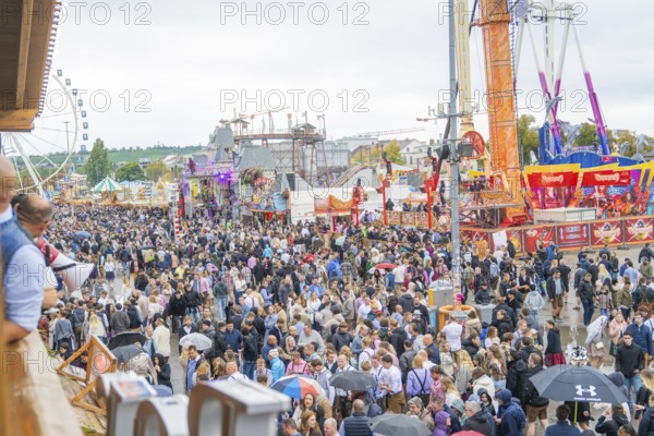 Large crowd at a folk festival with fairground rides under a cloudy sky, Cannstatter Wasen folk festival, Stuttgart, Germany