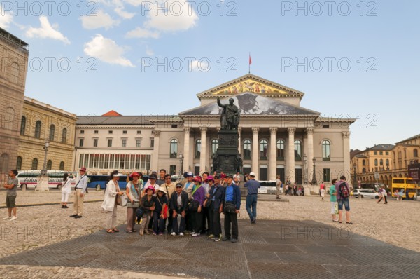 Japanese tourist group in front of the King Max I Joseph Monument. In the back National Theatre Bavarian State Opera, on the left Residenztheater and Residenz, Munich, Bavaria