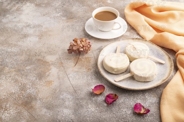 ?hocolate Ice cream in white glaze, cup of coffee, on brown concrete background and orange textile, side view, copy space, minimalism