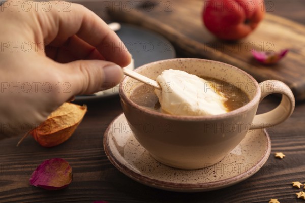 ?hocolate Ice cream in white glaze, cup of coffee, with hand on brown wooden background, side view, close up, selective focus