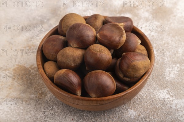 Wooden bowl with raw edible ?hestnuts on brown concrete background, side view, close up, minimalism
