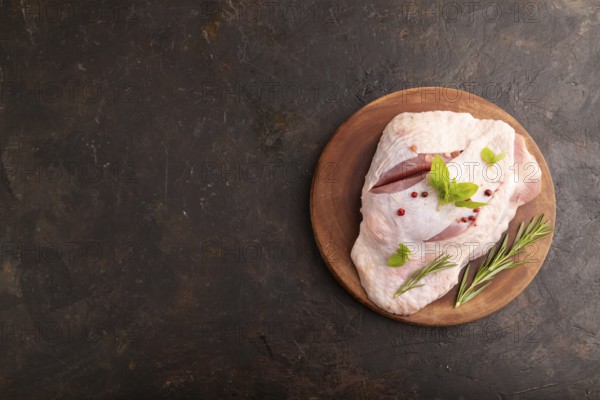 Raw Turkey Thigh with spices and rosemary on cutting board on black concrete background. top view, flat lay, copy space