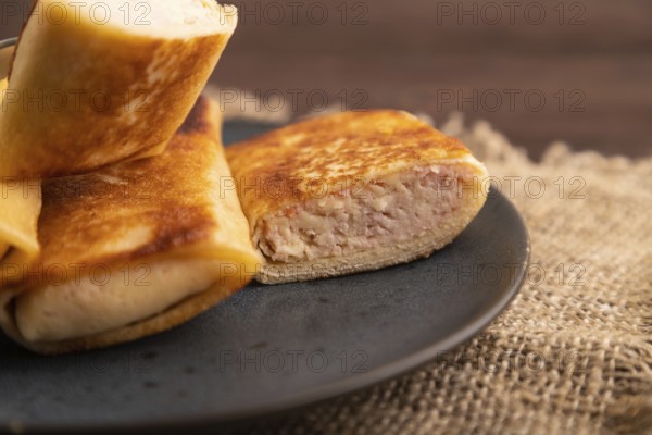 Fried crispy pancakes with meat and cheese on brown wooden background and linen textile. side view, close up, selective focus
