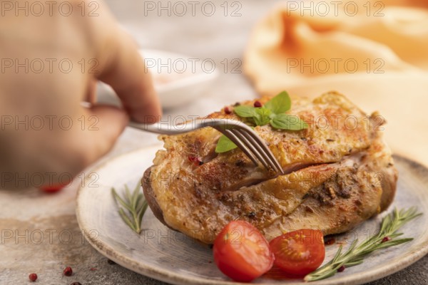 Fried Turkey Thigh with spices and rosemary on plate with hand on brown concrete background and orange linen textile. side view, close up, selective focus