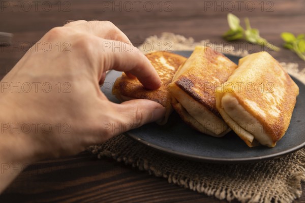 Fried crispy pancakes with meat and cheese with hand on brown wooden background and linen textile. side view, close up, selective focus