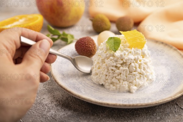 White ?ottage cheese, Curd, with orange and lychee with hand on brown concrete background and orange textile, side view, close up, selective focus