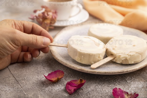 ?hocolate Ice cream in white glaze, cup of coffee, with hand on brown concrete background and orange textile, side view, close up, selective focus, minimalism