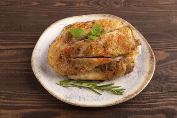 Fried Turkey Thigh with spices and rosemary on plate on brown wooden background. side view, close up
